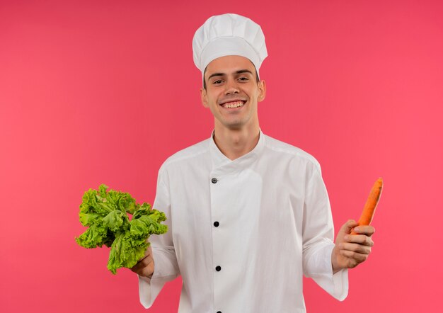 Free photo smiling young male cook wearing chef uniform holding salad and carrot