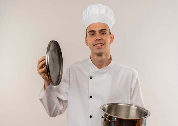 Smiling young male cook wearing chef uniform holding saucepan and lid