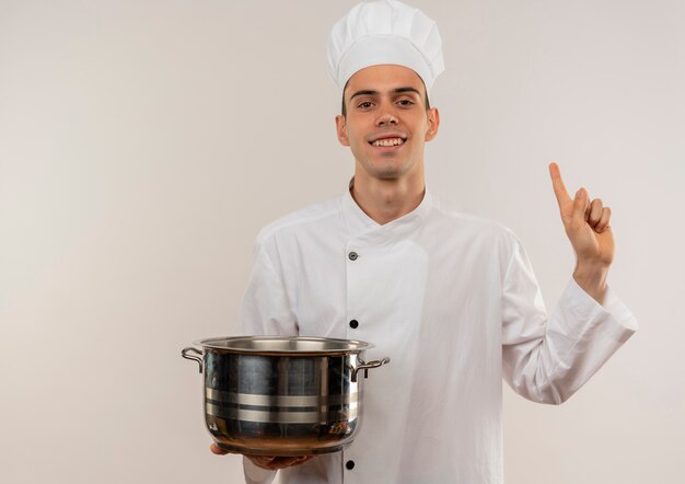 鍋を持っているシェフの制服を着て笑顔の若い男性料理人がコピースペースで指を上に向ける