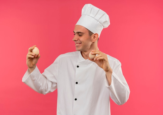 그의 손에 계란을보고 요리사 유니폼을 입고 웃는 젊은 남성 요리사