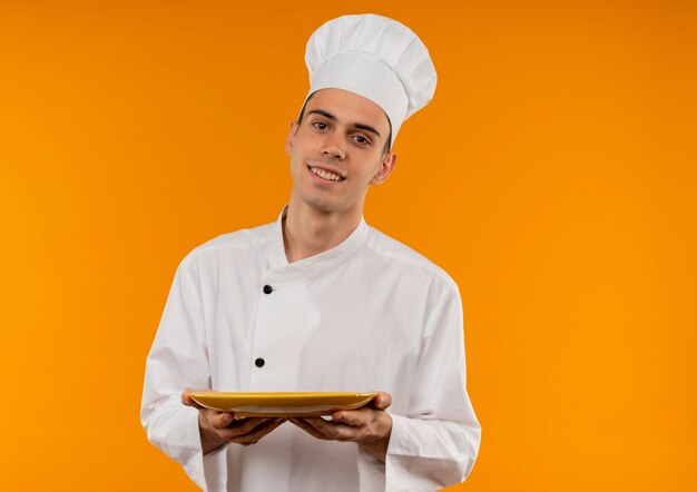 Smiling young male cool wearing chef uniform holding plate  with copy space