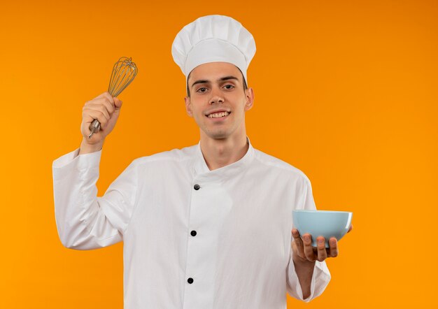 Smiling young male cool wearing chef uniform holding whisk and bowl 