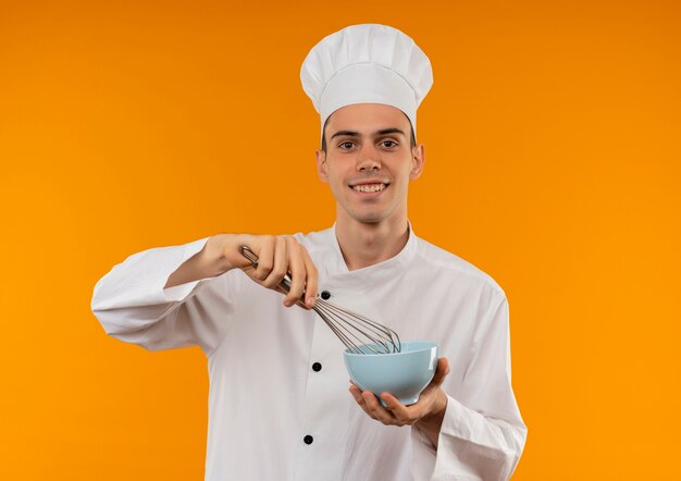 Smiling young male cool wearing chef uniform holding whisk and bowl 