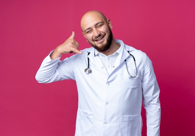 Smiling young male doctor wearing medical robe and stethoscope showing phone call