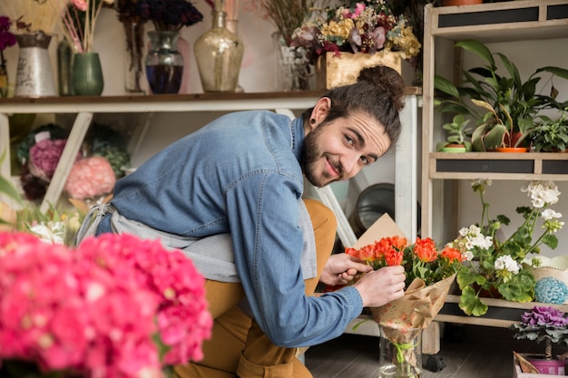 Foto gratuita giovane fiorista maschio sorridente che sistema il fiore nel mazzo