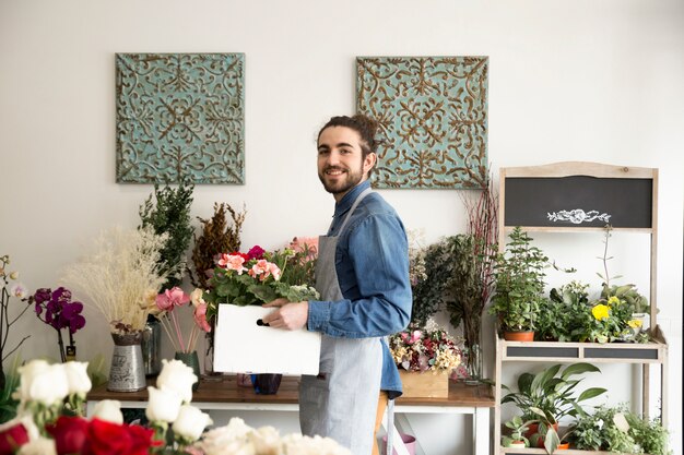 Smiling young male florist holding hydrangea plants in the wooden crate looking to camera