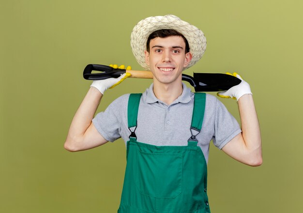 Улыбающийся молодой мужчина-садовник в садовой шляпе и перчатках держит лопату за шеей