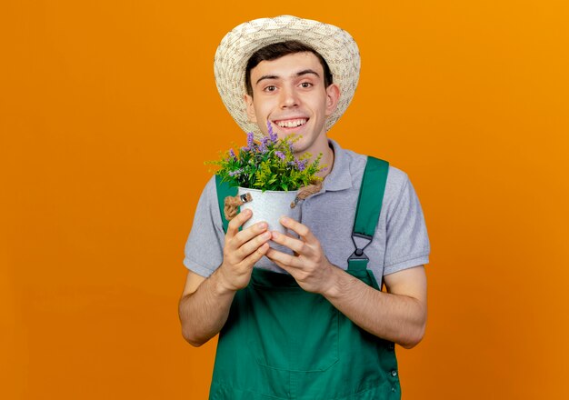 ガーデニング帽子をかぶって笑顔の若い男性の庭師は植木鉢に花を保持します