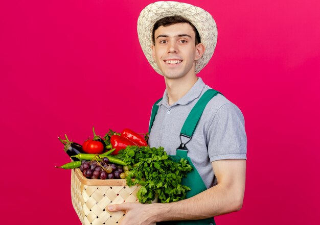 Улыбающийся молодой мужчина-садовник в садовой шляпе держит корзину с овощами