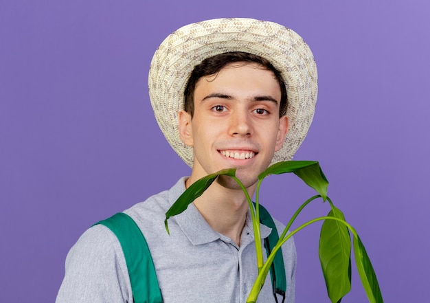 원예 모자를 쓰고 웃는 젊은 남성 정원사는 식물과 함께 서있다.
