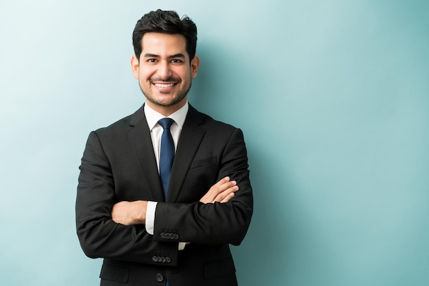 Smiling young male professional standing with arms crossed while making eye contact against isolated background