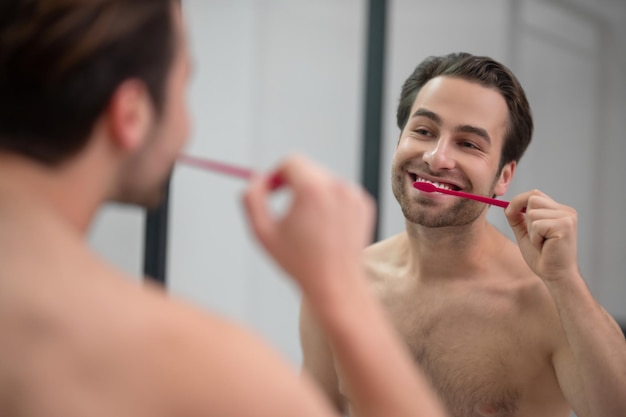 Smiling young man brshing his teeth and looking carefree