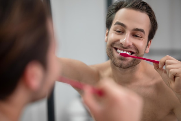 Smiling young man brshing his teeth and looking carefree