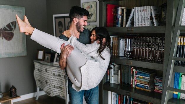 Smiling young man carrying her girlfriend in living room