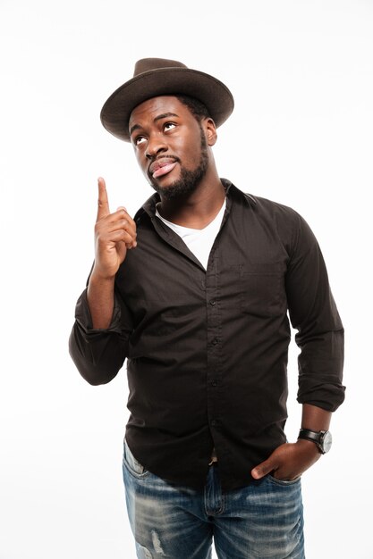 Smiling young man dressed in shirt wearing hat pointing.