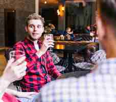 Free photo smiling young man drinking the beer with his friends in pub