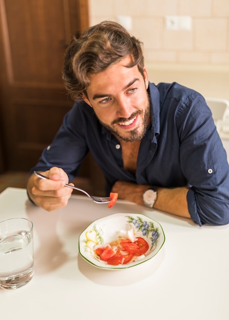 Free photo smiling young man eating salad with fork