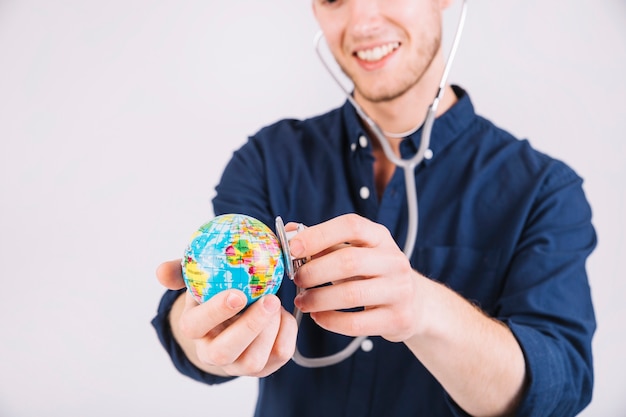 Smiling young man examining globe with stethoscope