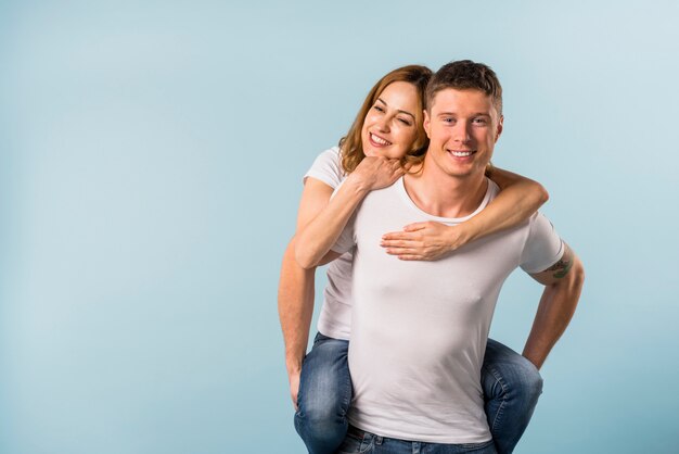 Smiling young man giving piggyback ride to her girlfriend against blue backdrop