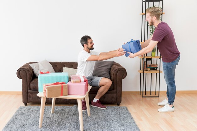 Smiling young man giving present box to his friend at home