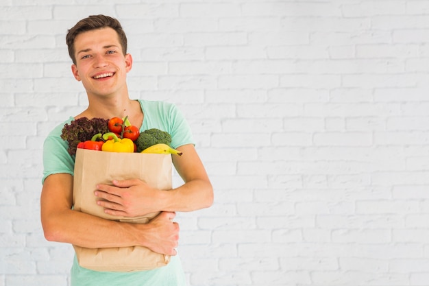 新鮮な野菜や果物を食料紙の袋に入れて笑っている若い男