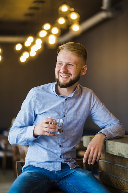 Smiling young man holding glass of drink at restaurant