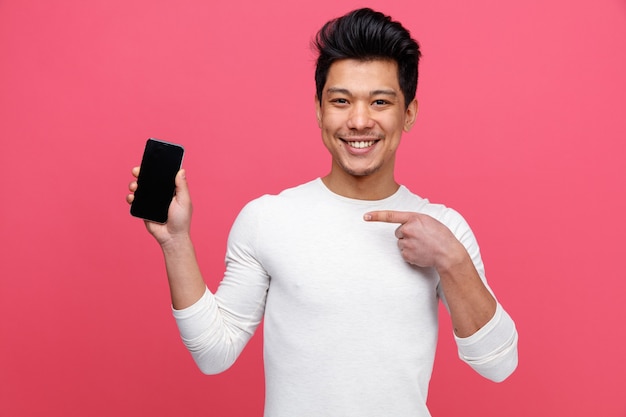 Giovane sorridente che tiene e che indica al telefono cellulare