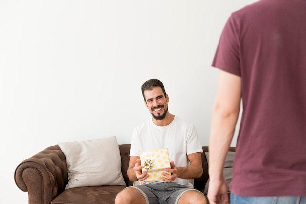 Smiling young man holding polka dot wrapped gift box with his friend