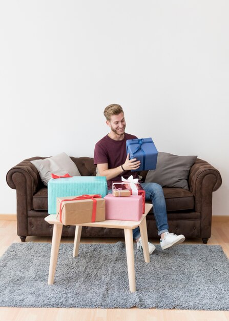 Smiling young man holding present box sitting on sofa at home