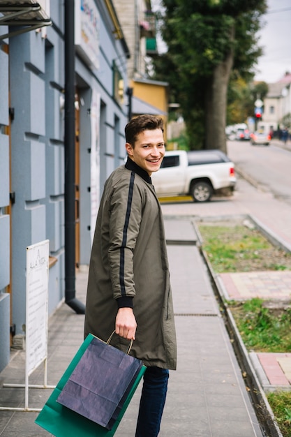 Smiling young man holding shopping bags looking over shoulder