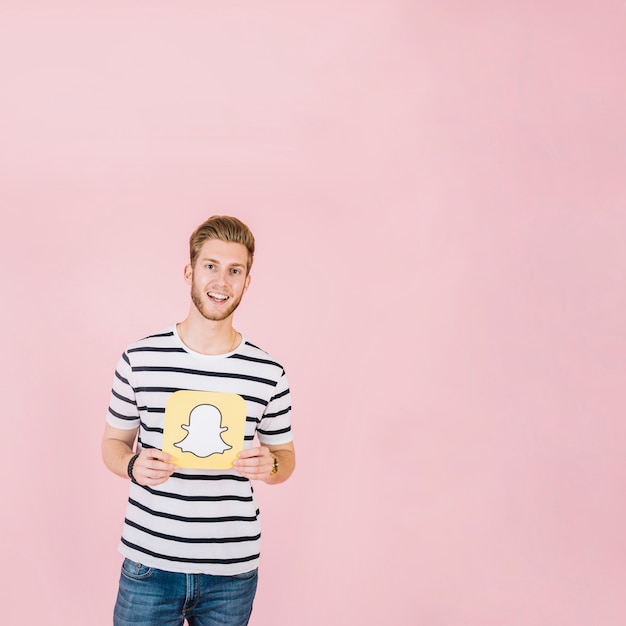 Free photo smiling young man holding snapchat icon on pink background