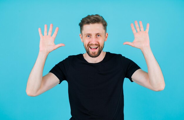 Smiling young man is raising up his handfuls on blue background