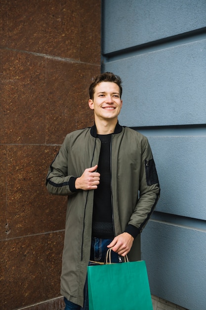 Free photo smiling young man in long jacket holding green shopping bag