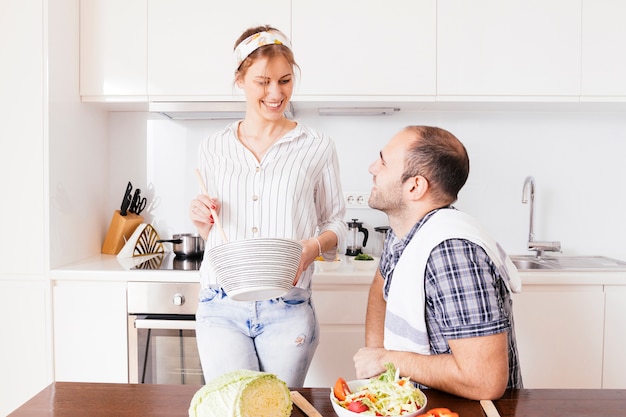 Foto gratuita giovane sorridente guardando sua moglie a preparare il cibo in cucina