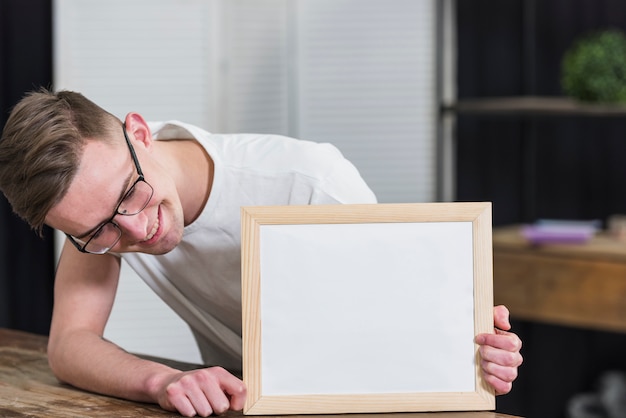 Foto gratuita giovane sorridente che esamina il bordo di legno bianco sul tavolo