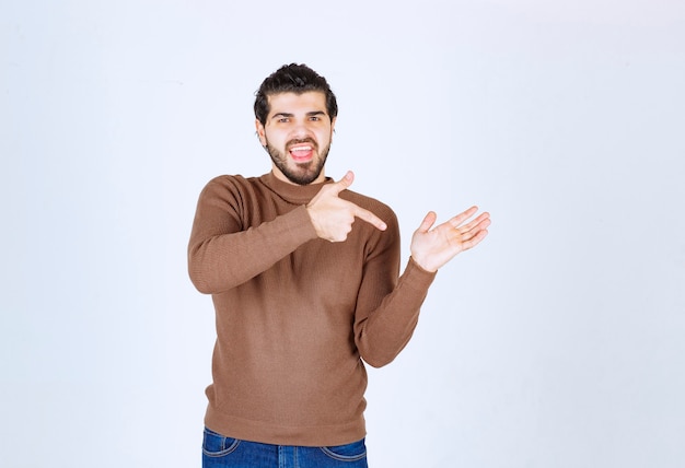 A smiling young man model wearing brown sweater pointing at his palm. High quality photo