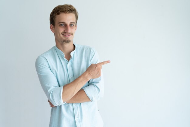 Smiling young man pointing finger aside. Handsome guy recommending something.