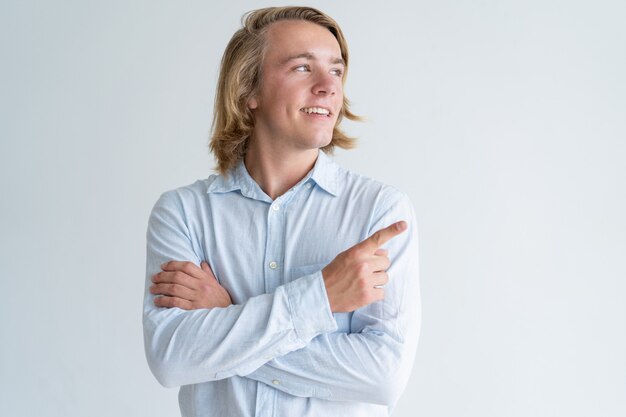 Smiling young man pointing finger aside