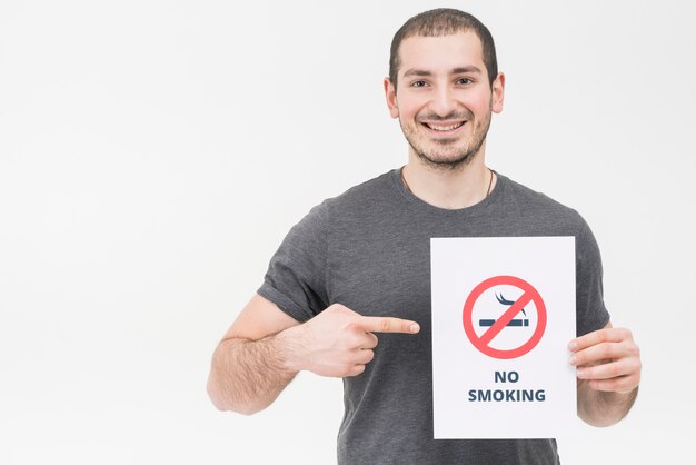 Улыбающийся молодой человек, указывая пальцем на знак не курить на белом фоне