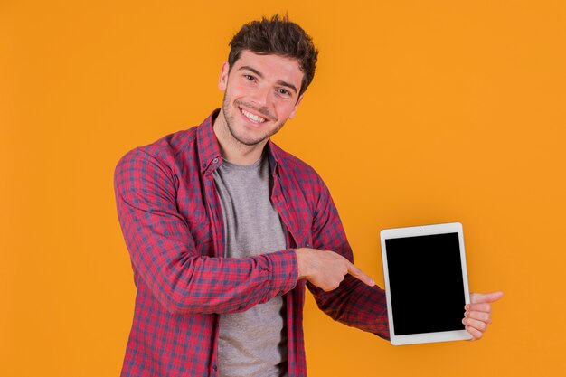 Улыбающийся молодой человек, указывая пальцем на цифровой планшет на оранжевом фоне