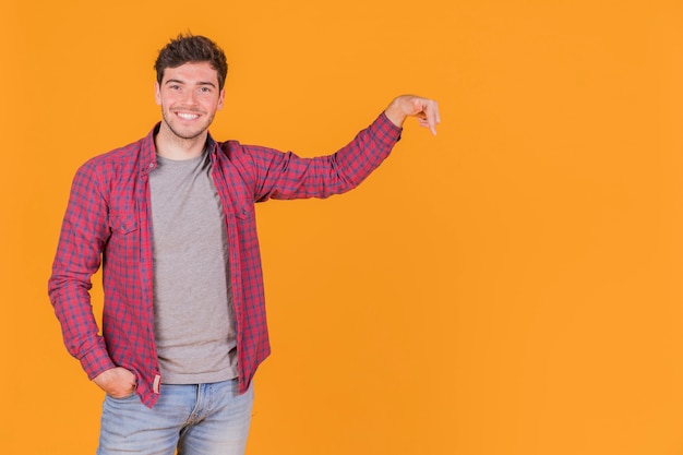 Улыбающийся молодой человек, указывая пальцем вверх на оранжевом фоне