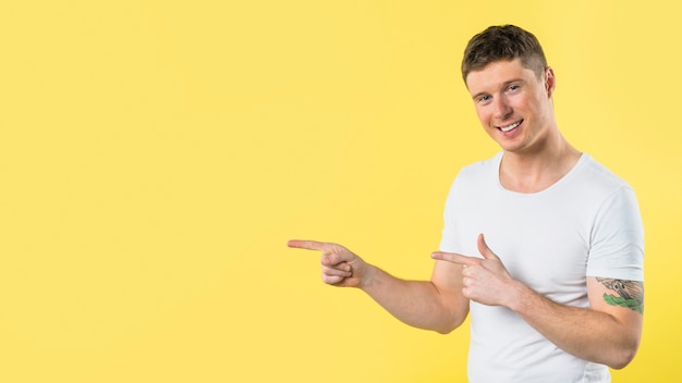 Smiling young man pointing his fingers against yellow background