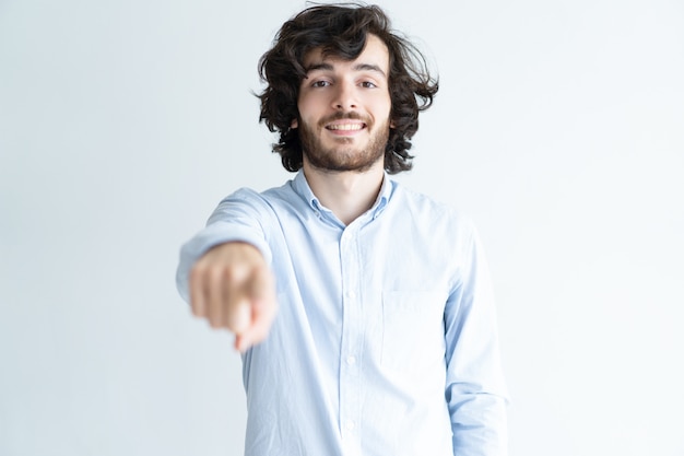 Free photo smiling young man pointing at viewer and looking at camera