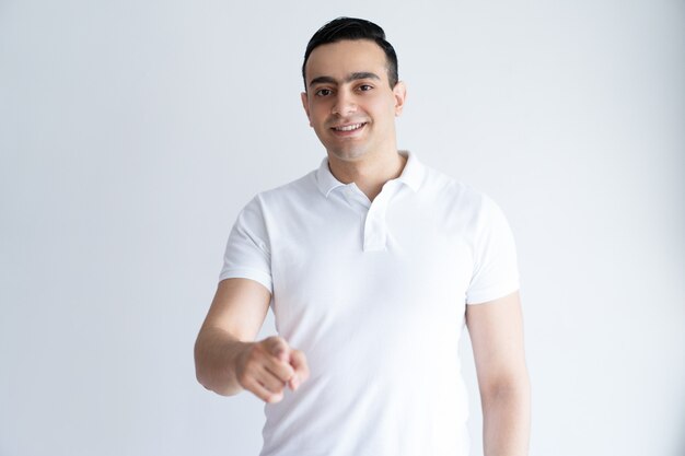 Smiling young man pointing at you and looking at camera. Guy choosing viewer.