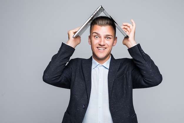 Smiling young man posing with laptop on his head dressed up in dark jacket in studio isolated on grey wall