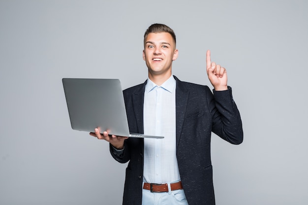 Smiling young man posing with laptop phone dressed up in dark jacket in studio isolated on grey wall