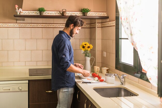 Smiling young man preparing salad in the kitchen