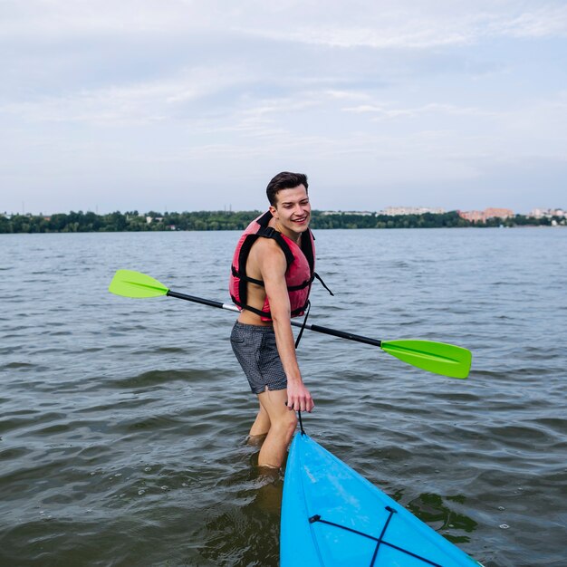 Smiling young man pulling kayak on lake