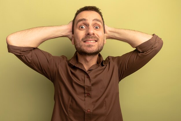 Free photo smiling young man putting hands behind head looking at front isolated on olive green wall