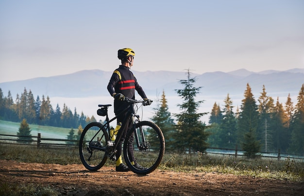 Free photo smiling young man riding bicycle on mountain road